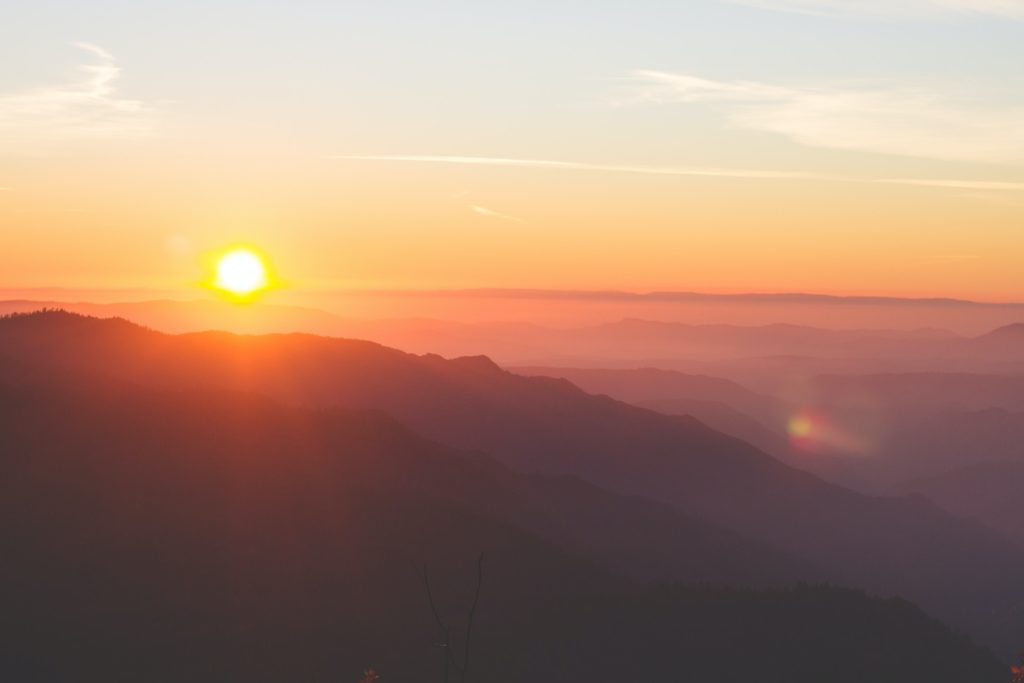 The rising sun shines bright orange over a valley with a morning prayer for peace.