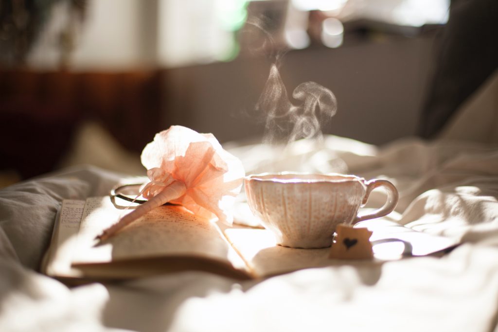 A steaming cup of tea sits on an open journal with a flowery pen waiting for a morning prayer about rest to be written.