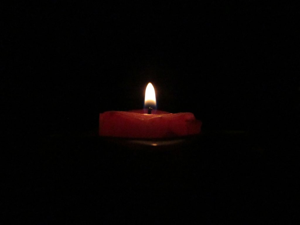 A lit candle in the darkness illustrates finding joy in our trials.