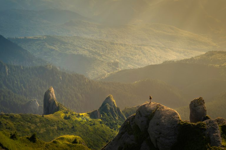 A small figure stands on a green hill in the mountains pondering the connection between truth and faith.