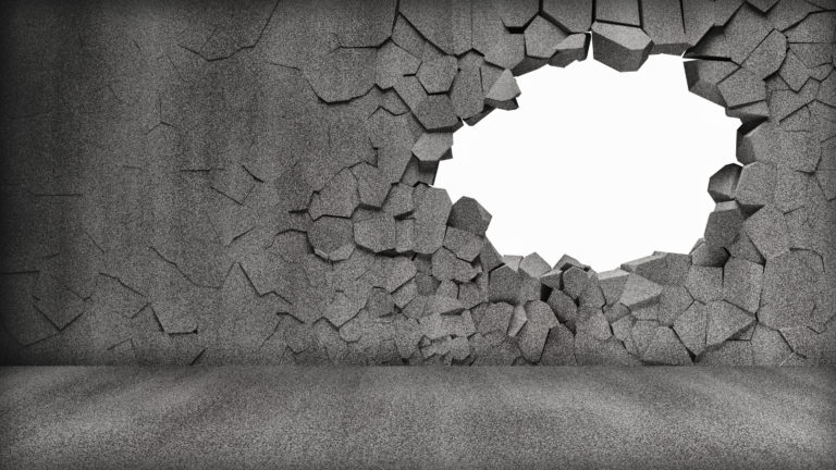 A large hole broken into a concrete wall starts the process of deconstruction.