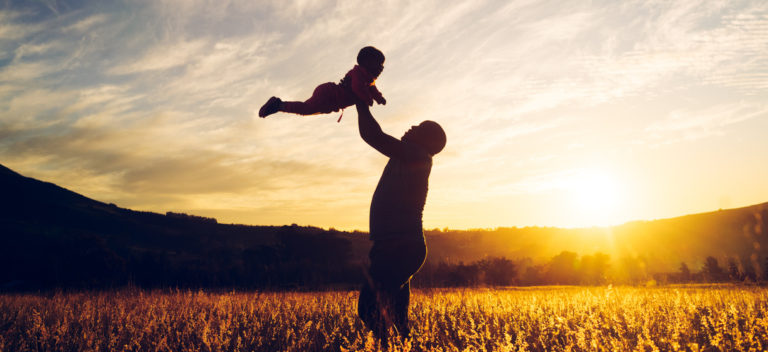 A man in silhouetted swings a child up in the air in a field at sunset reminding us that our Father's love is stronger than fear.