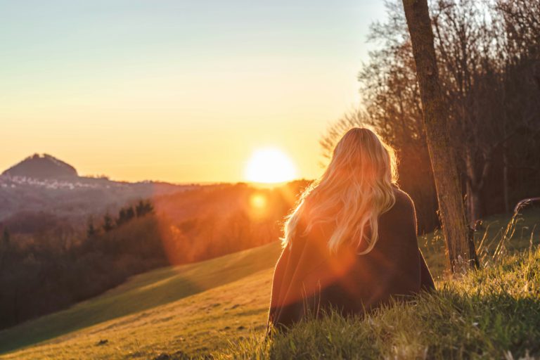 A young blonde woman sits on a mountain at sunset knowing that she's sealed as God's own.
