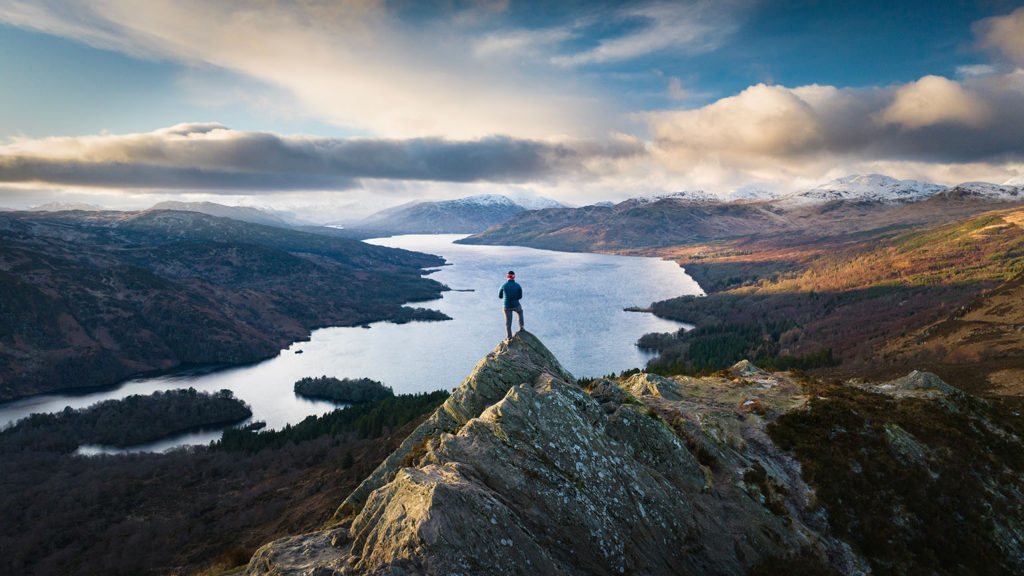 A man stands in silhouette at sunset overlooking a river in the hills wondering how to help you be your authentic self.