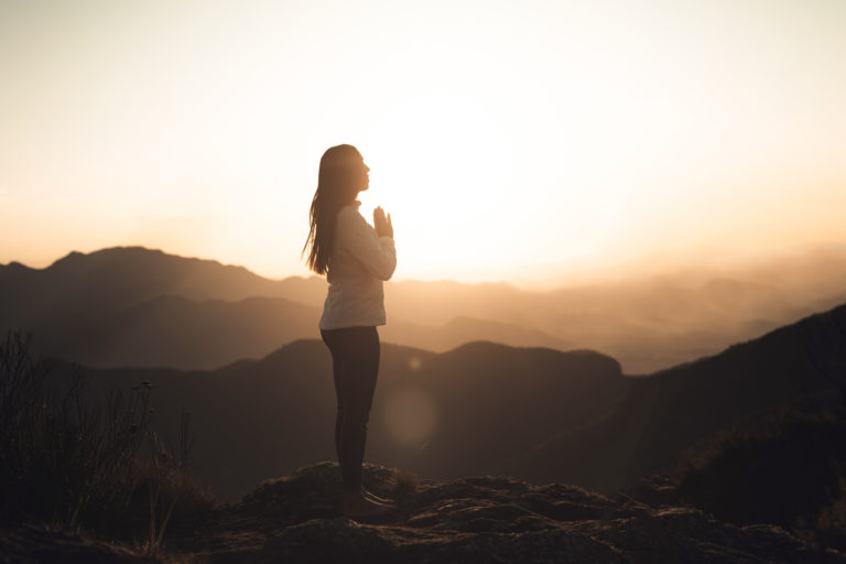 A woman stands on a mountain at sunset reflecting on the revelations that transformed her life.