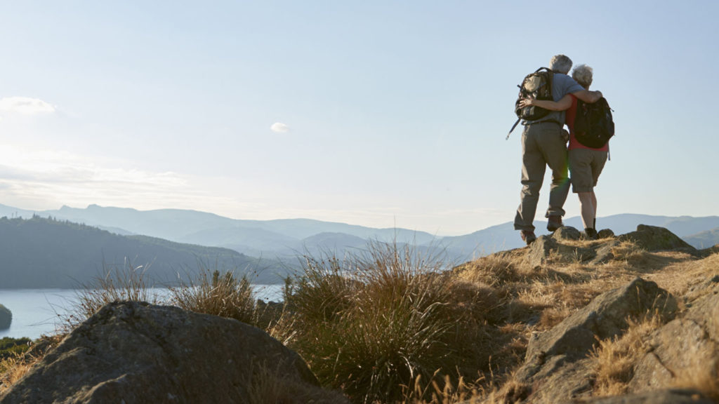 A couple stands on the top of a hill overlooking a lake as the helped bear each others' burdens.