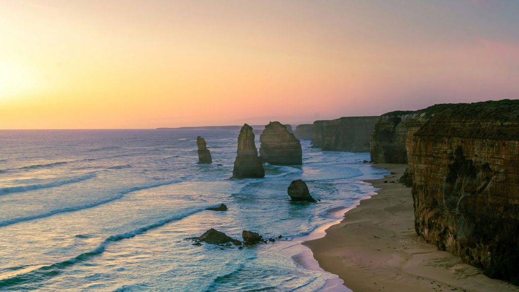 Rocks stick out of the ocean near the shore during sunset cultivating a glad heart.