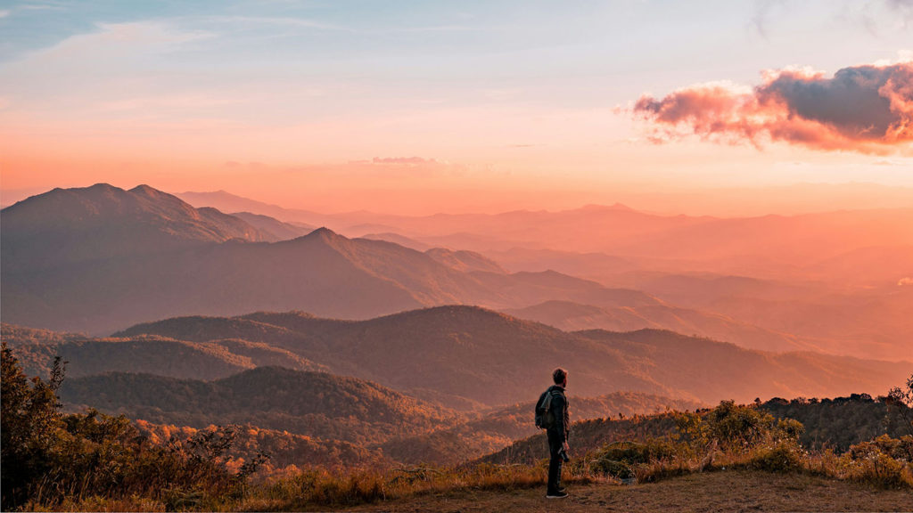 A man in silhouette stands on a mountain at sunset knowing it's okay for him to weep, laugh, mourn and dance.