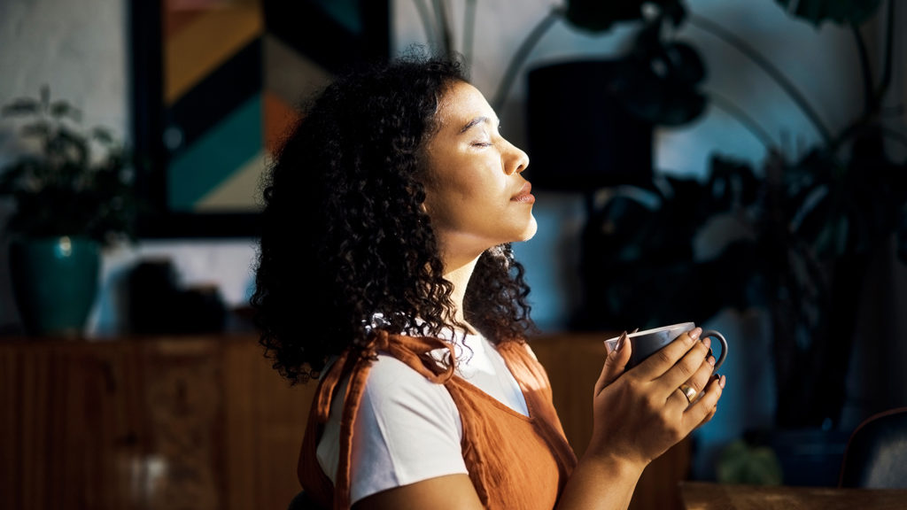 A woman with her eyes closed turns off her mind and holds a cup of coffee