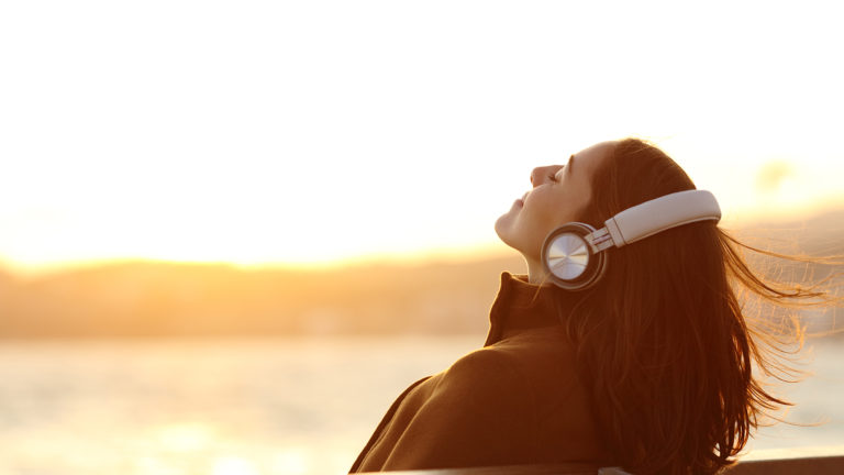 Woman listens to soundscapes while sitting on a bench at sunrise