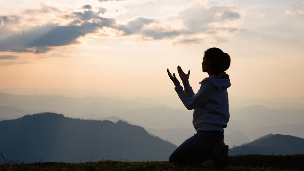 Silhouette of a woman with hands raised in the sunset as she learns about listening to God.