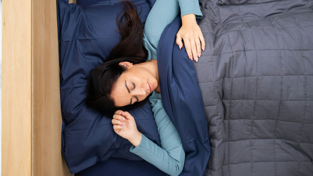 A young woman sleeps peacefully covered by a dark comforter as she experiences the spiritual benefits of sleep.